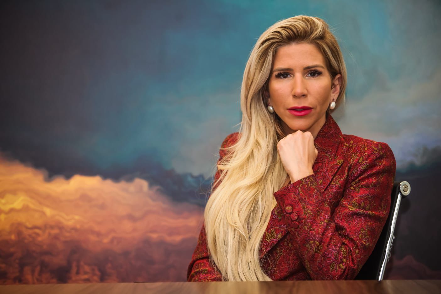 A autora, de blazer vermelho, em pose reflexiva